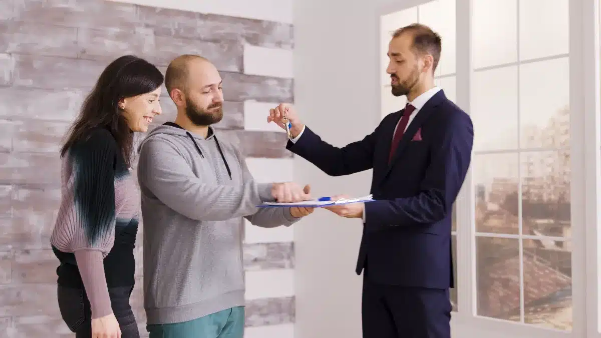 סוכן נדל״ן מציג מסמכי עסקה לזוג רוכשים בתוך דירה